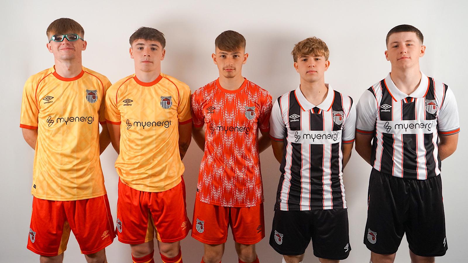 Five young men pose in matching sports kits. Three wear orange and red kits, and two wear black and white striped kits.