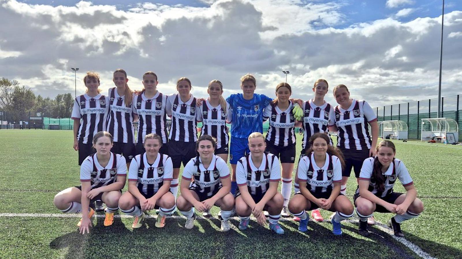 A women's soccer team in black and white striped jerseys poses on a field under a cloudy sky.