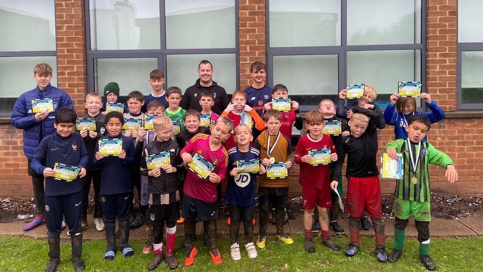 A group of children holding up books in front of a building.