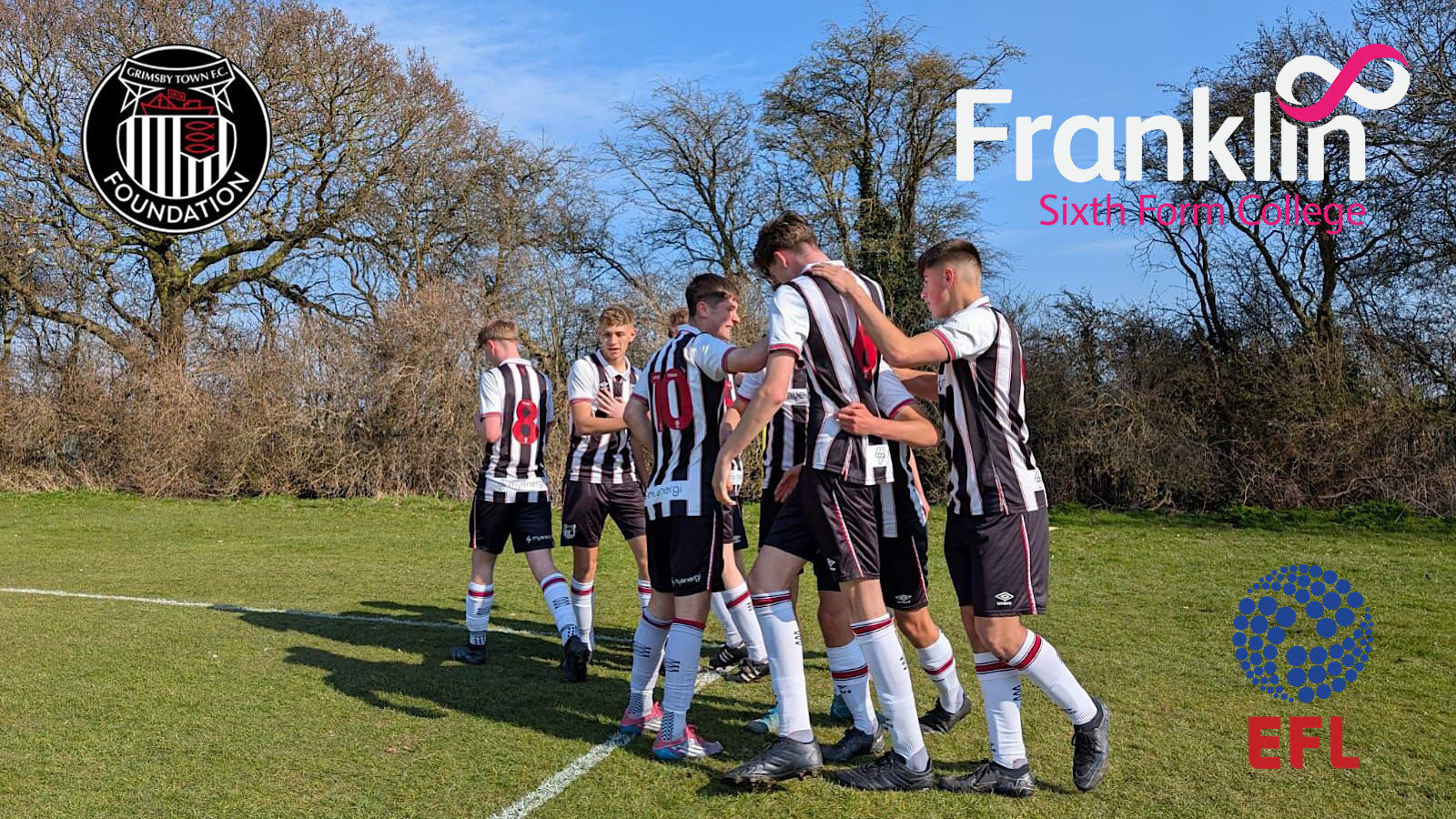 A group of soccer players in black and white striped uniforms stands in a circle on a grassy field. Logos for Grimsby Town Foundation, Franklin Sixth Form College, and EFL are visible.