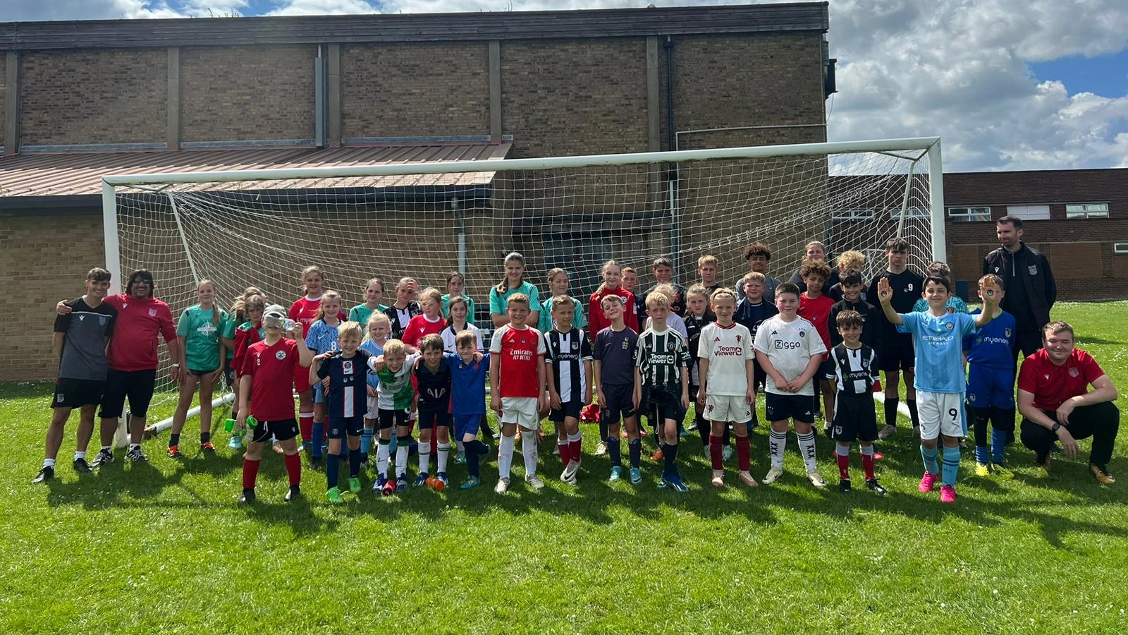 A group of children and adults in soccer uniforms posing in front of a goal on a grassy field.