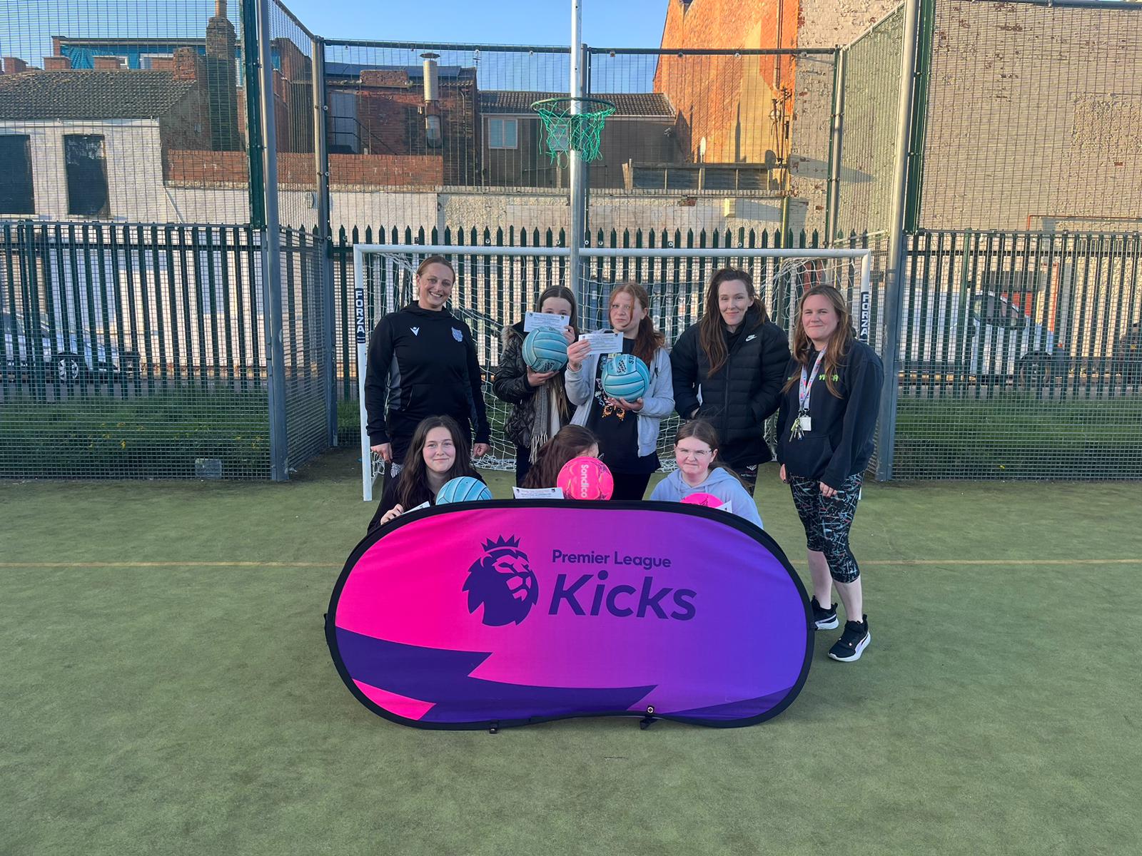 Group of young people posing with a "premier league kicks" sign on a basketball court.