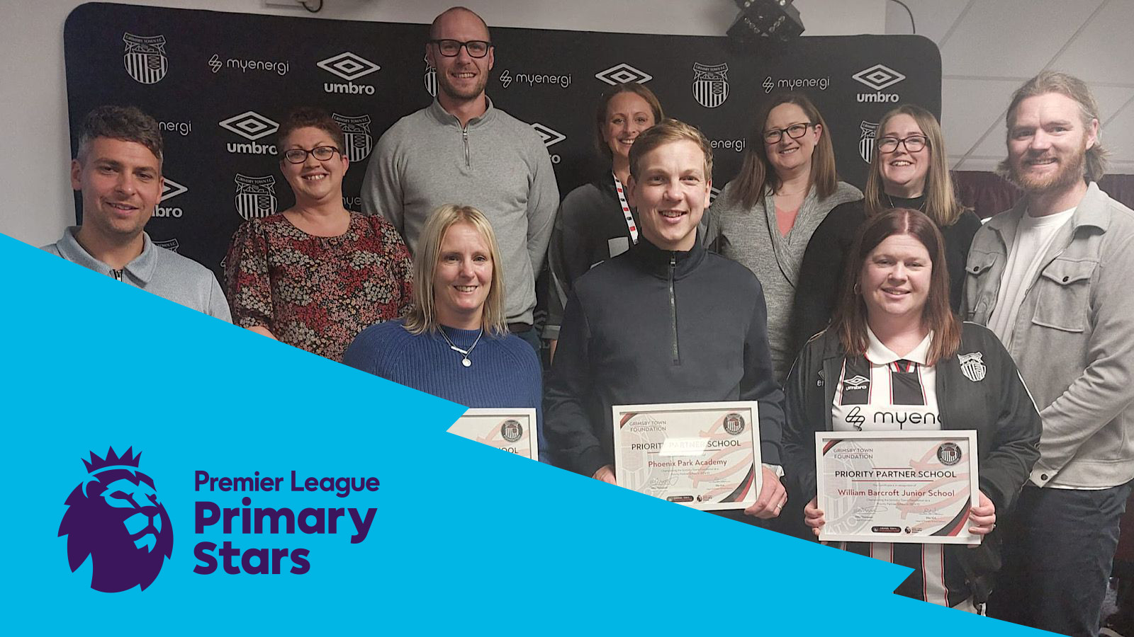 Group of people posing with certificates in front of a Premier League Primary Stars banner.